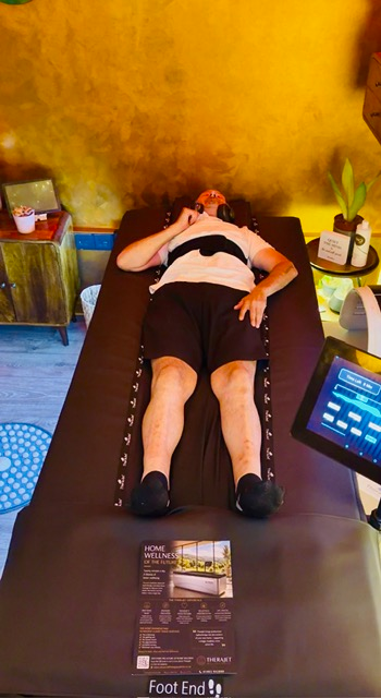 A guest lying fully clothed on the TheraJet dry hydrotherapy table beside the touchscreen control panel